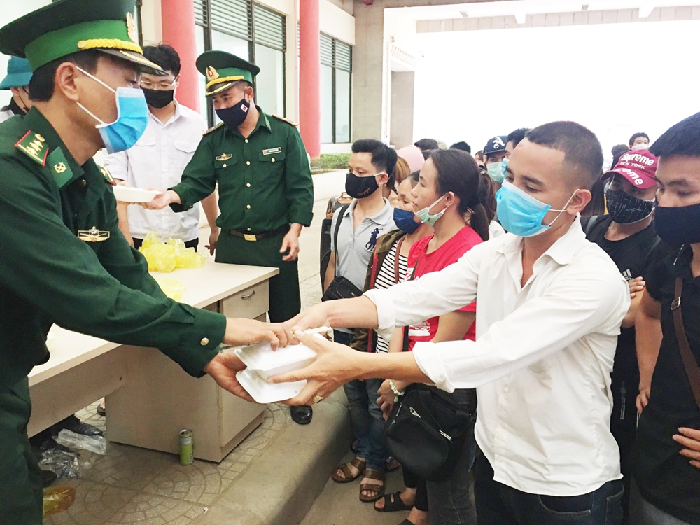 Cán bộ, chiến sĩ Đồn Biên phòng CKQT Cha Lo phát cơm tới người nhập cảnh trong khi chờ thủ tục để đi cách ly 14 ngày theo quy định. Ảnh: Bùi Toàn.